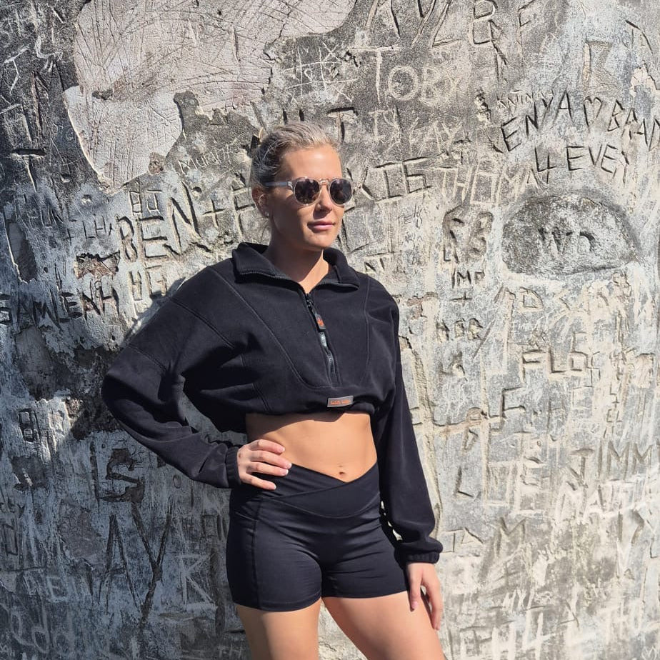 Person wearing a black jacket and shorts standing against a wall with engraved text.